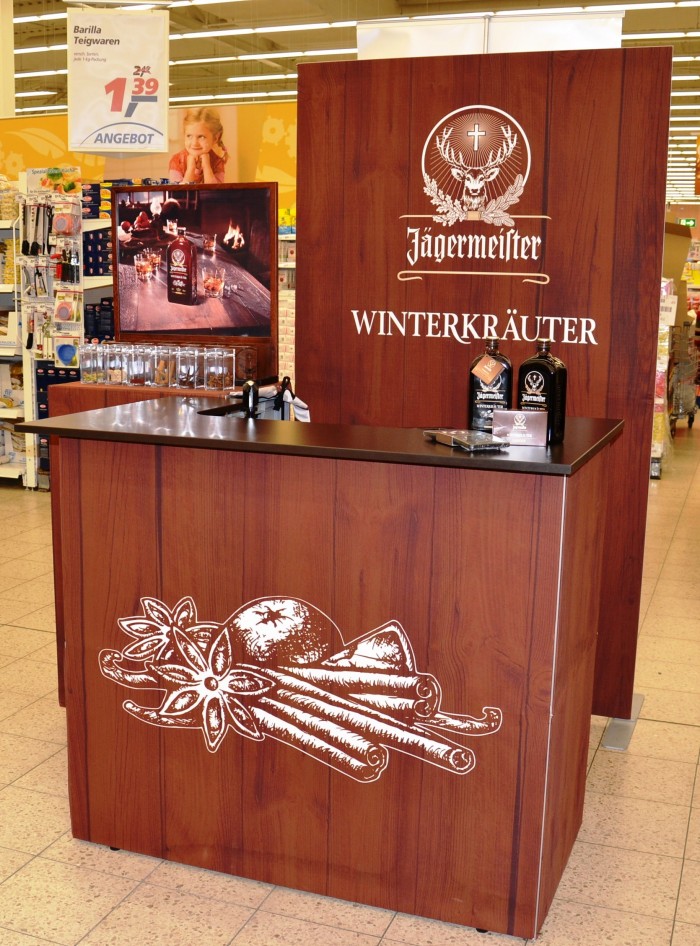 Messetheke von Jägermeister mit dem Schriftzug 'WINTERKRÄUTER' und dekorativen Kräutermotiven, in einem Verkaufsraum.