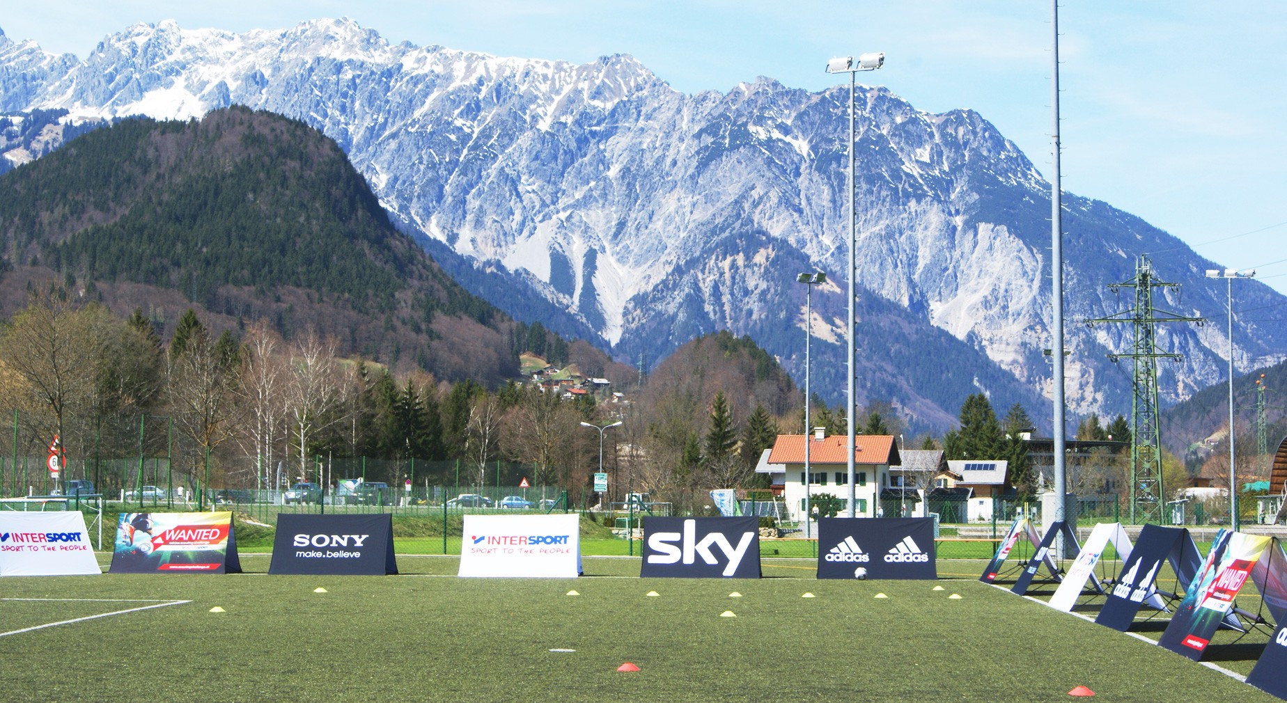 Werbebanner am Fußballplatz mit Bergen im Hintergrund, Marken wie Sky, Adidas und Sony sichtbar.