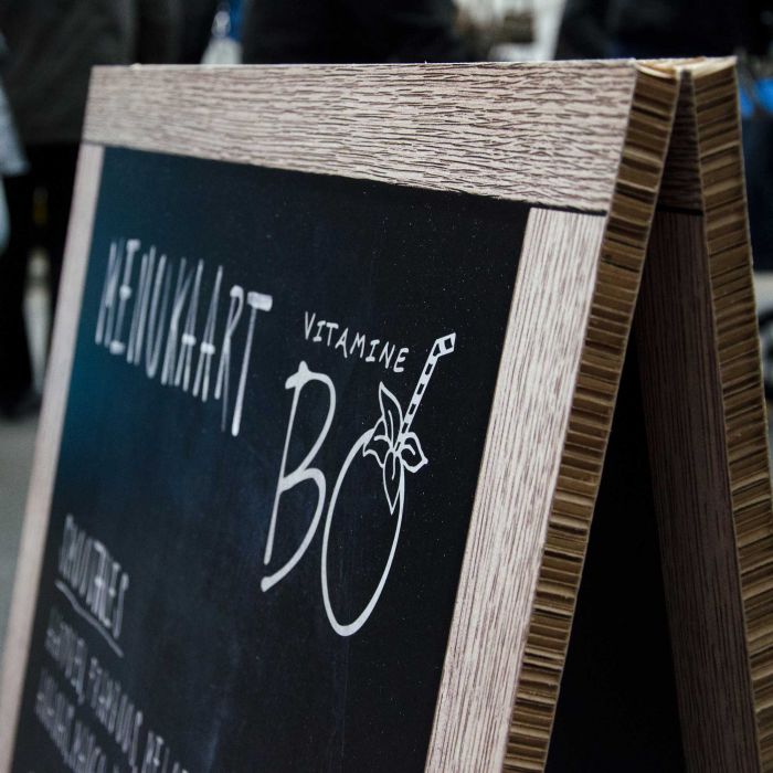 Reboard Speisekarte mit der Aufschrift 'HEIMAT' und 'VITAMINE BO', auf einem Holzständer.