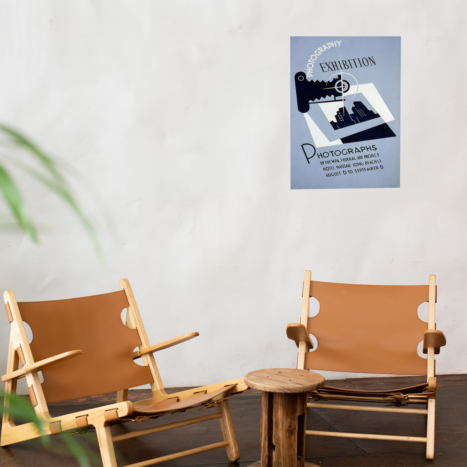 Plakat mit dem Text 'PHOTOGRAPHY EXHIBITION' an einer Wand über zwei Holzstühlen und einem Tisch.