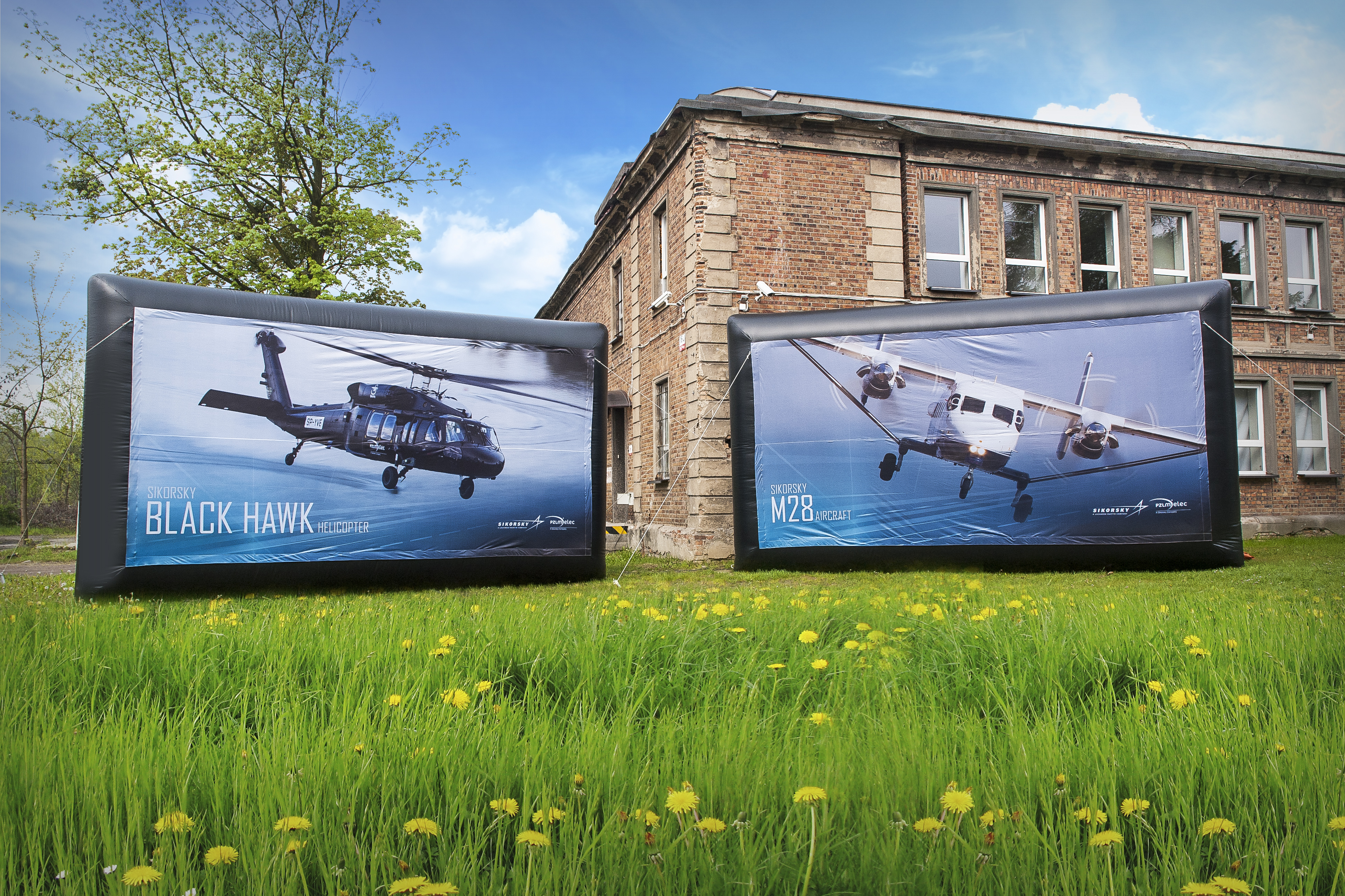 Aufblasbare Werbewand mit den Helikoptern Black Hawk und M28, auf einer Wiese vor einem historischen Gebäude.