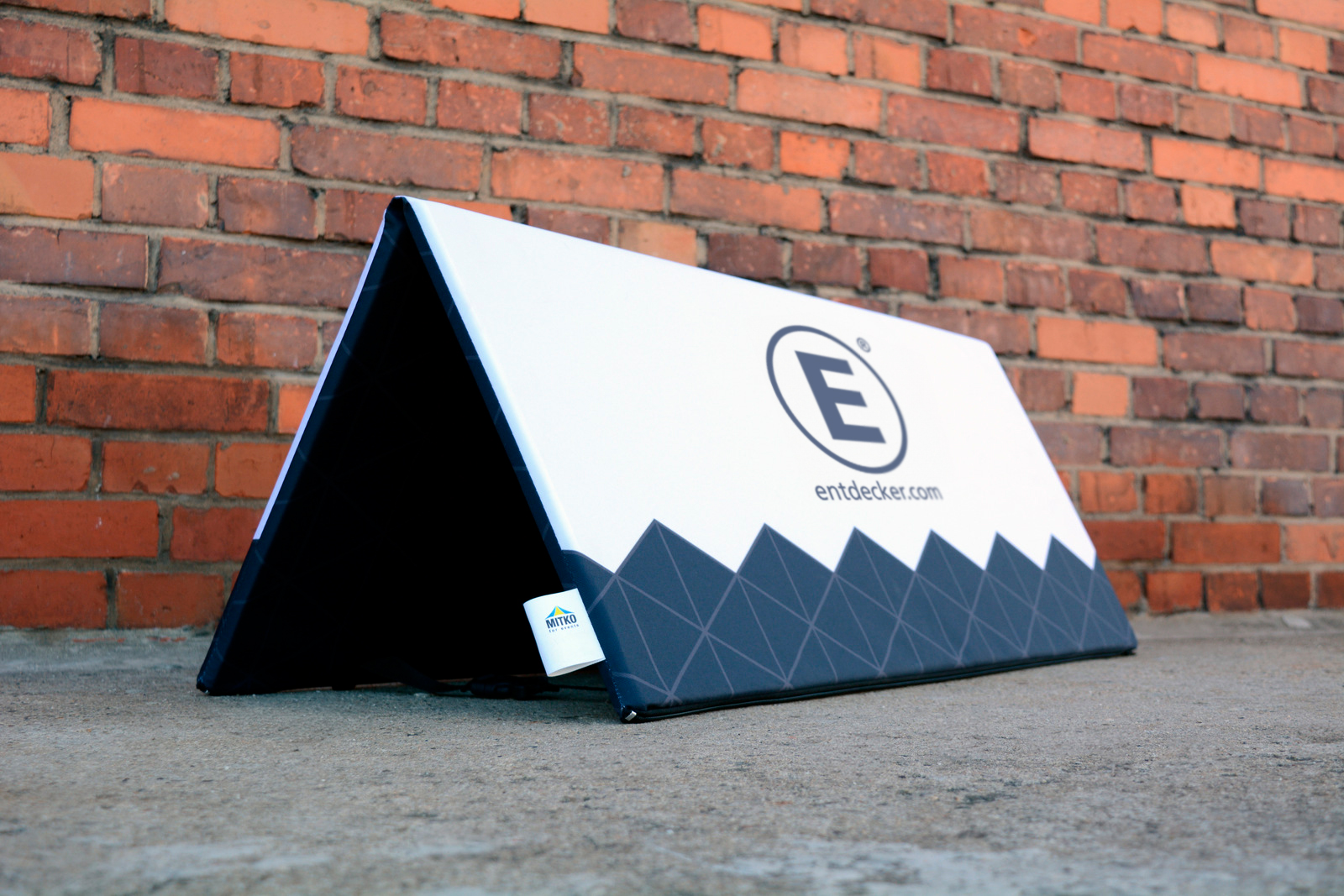 Faltbare Softbande von ENTDECKER, schwarz mit geometrischem Muster und Logo, auf einem Betonboden vor einer Ziegelwand.