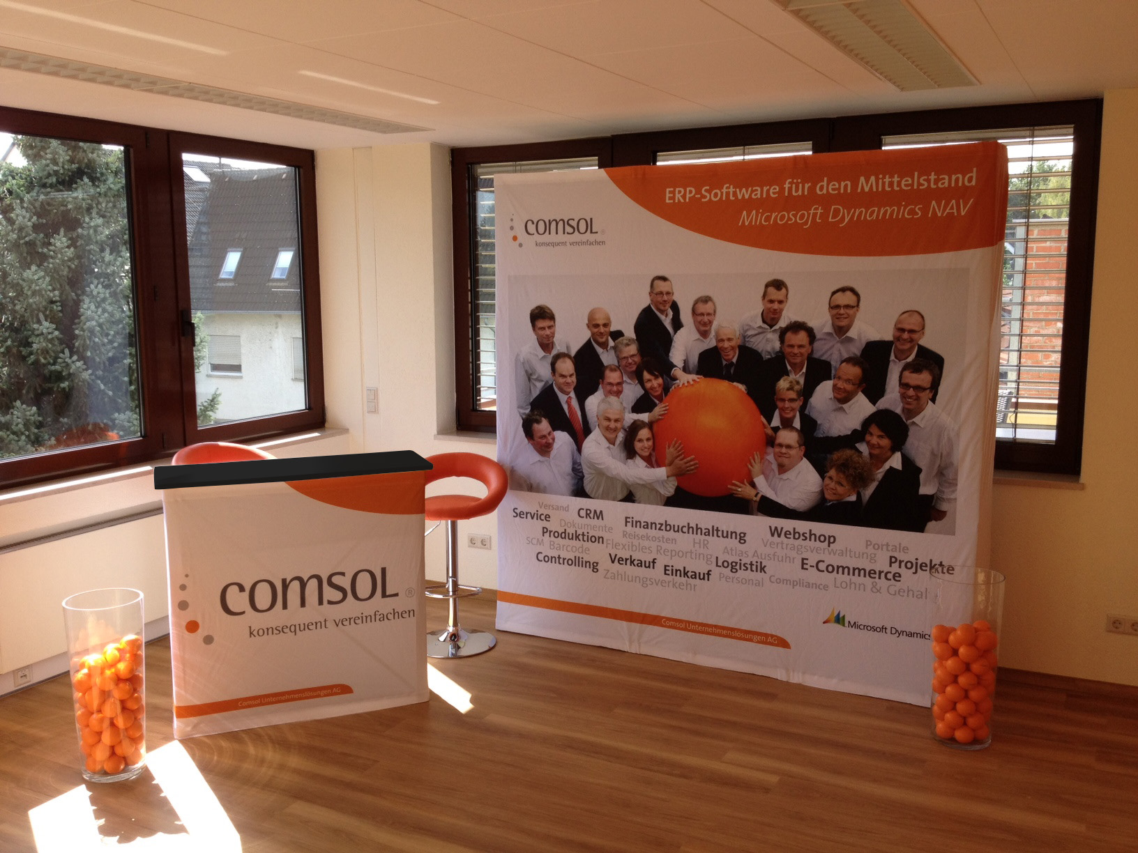 Falttheke mit Messewand von COMSOL, präsentiert ERP-Software für den Mittelstand, mit orangefarbenem Ball und Teamfoto.