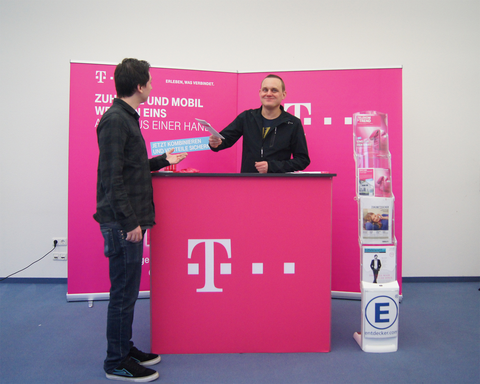 Mitarbeiter am Telekom Messestand übergibt Informationsmaterial an einen Besucher.