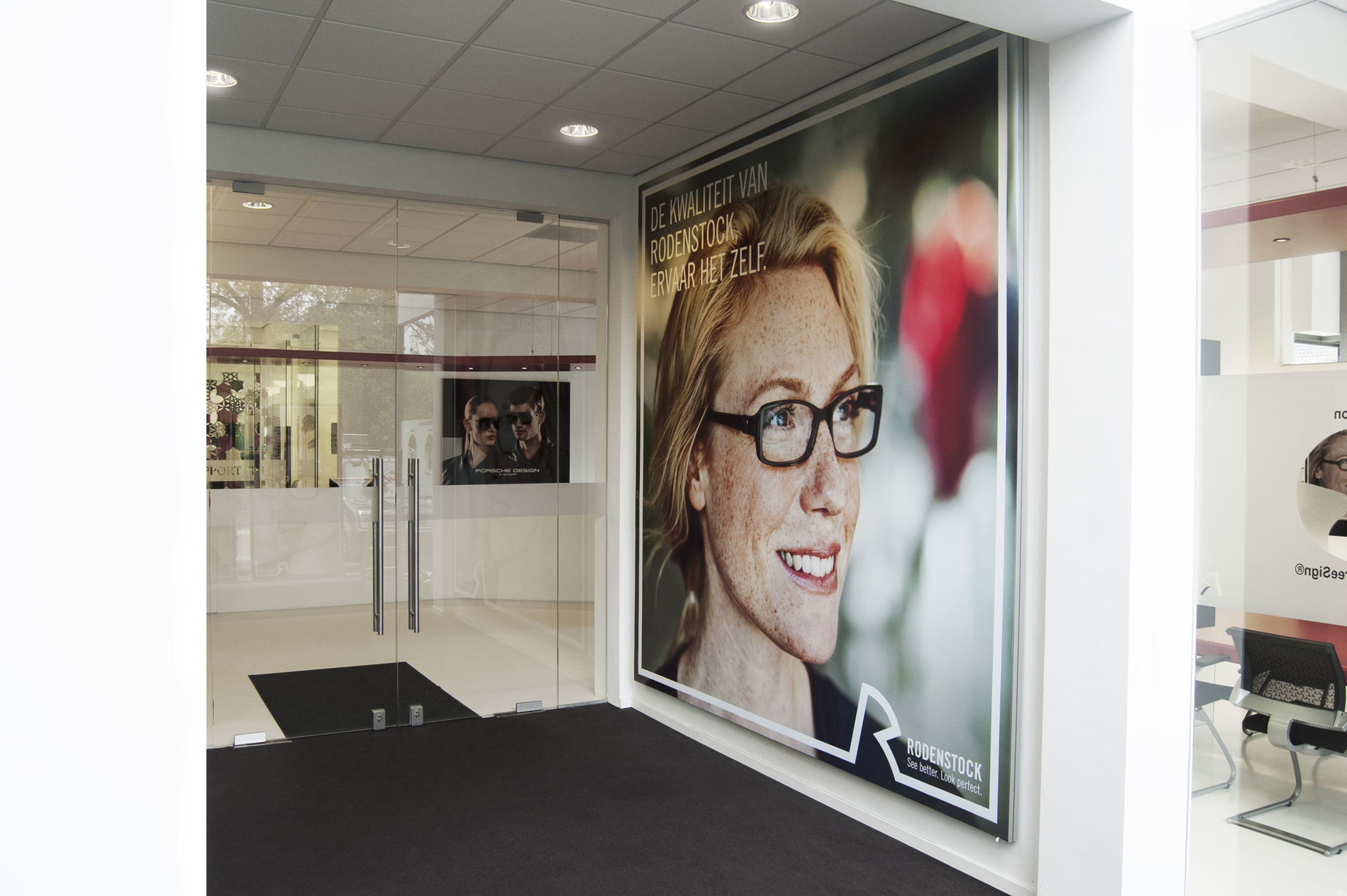 Textilspannrahmen von Rodenstock am Eingang eines Geschäfts, mit einem großen Werbebild einer Brillenträgerin im Hintergrund.